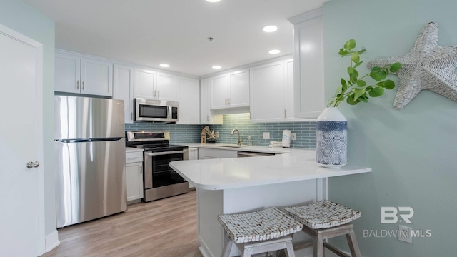 kitchen featuring a peninsula, a sink, stainless steel appliances, light countertops, and backsplash