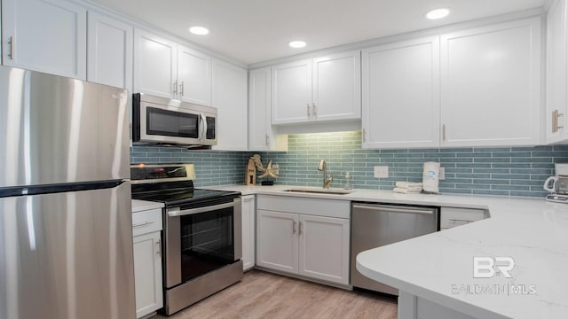 kitchen with a sink, appliances with stainless steel finishes, white cabinets, light wood finished floors, and decorative backsplash