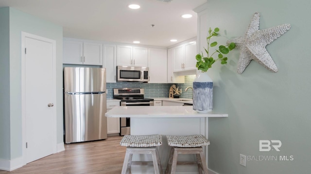 kitchen with a sink, appliances with stainless steel finishes, a peninsula, light countertops, and decorative backsplash