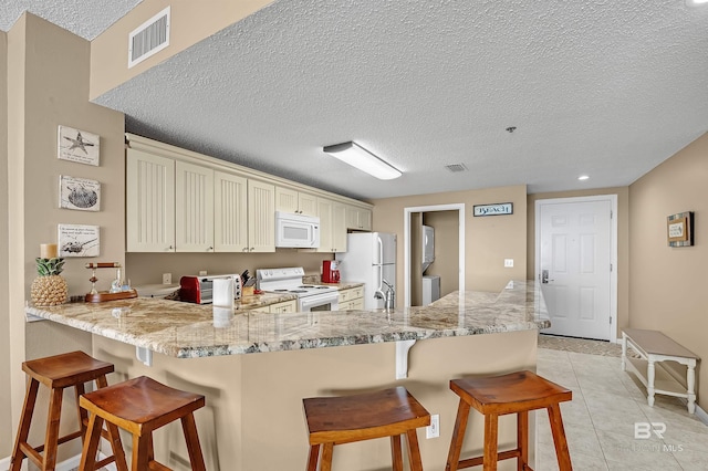 kitchen featuring a kitchen bar, white appliances, a peninsula, and visible vents