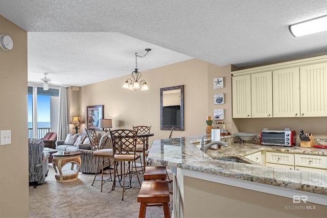 kitchen featuring decorative light fixtures, open floor plan, light carpet, cream cabinets, and a sink