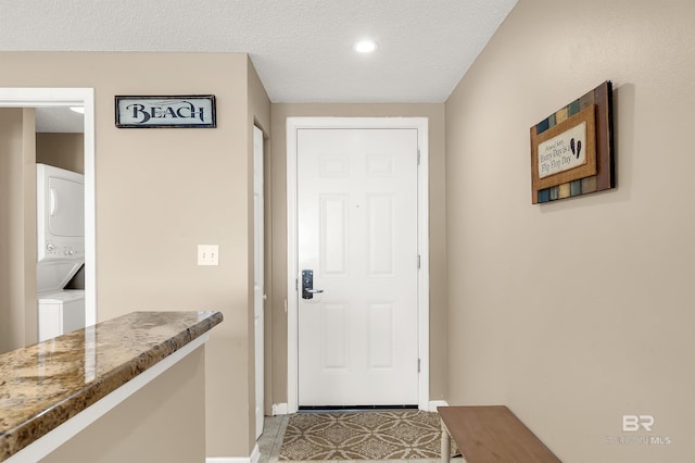 doorway featuring recessed lighting, a textured ceiling, baseboards, and stacked washer and dryer