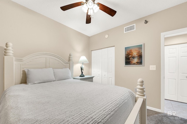 carpeted bedroom with a ceiling fan, baseboards, visible vents, and multiple closets