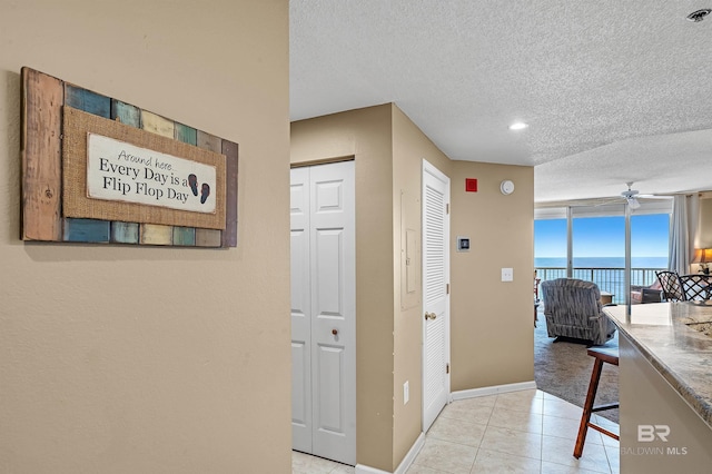 corridor featuring light tile patterned floors, a textured ceiling, baseboards, and a water view