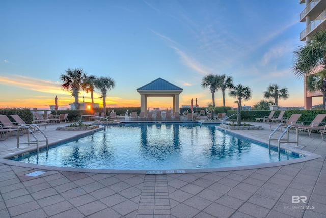 pool at dusk with a community pool and a patio area