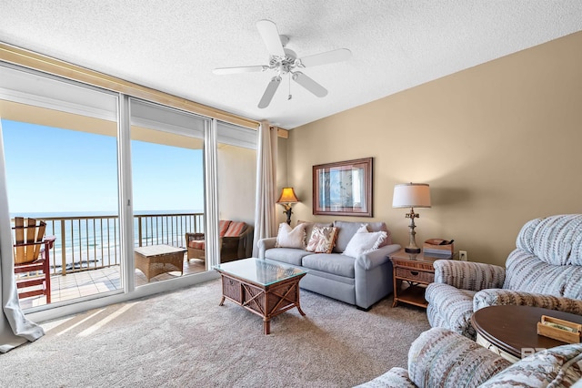 living room with a textured ceiling, carpet flooring, a water view, and ceiling fan