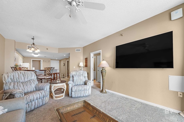 carpeted living room featuring visible vents, baseboards, a textured ceiling, and ceiling fan with notable chandelier