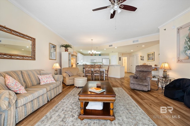 living room with ceiling fan with notable chandelier, ornamental molding, light wood-type flooring, and visible vents