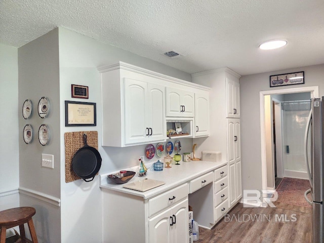 kitchen with white cabinetry, hardwood / wood-style flooring, stainless steel refrigerator, and a textured ceiling