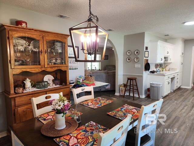 dining area featuring a textured ceiling, dark wood-type flooring, and an inviting chandelier