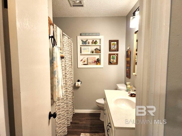 bathroom featuring wood-type flooring, toilet, a textured ceiling, and vanity