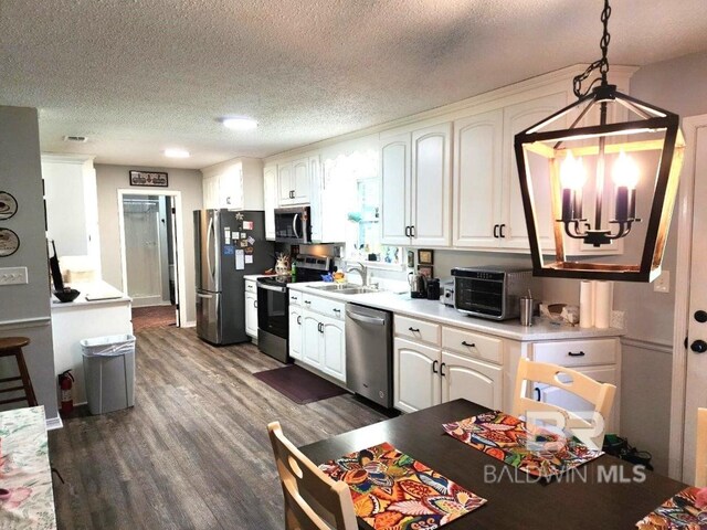 kitchen with stainless steel appliances, decorative light fixtures, hardwood / wood-style floors, white cabinetry, and a textured ceiling