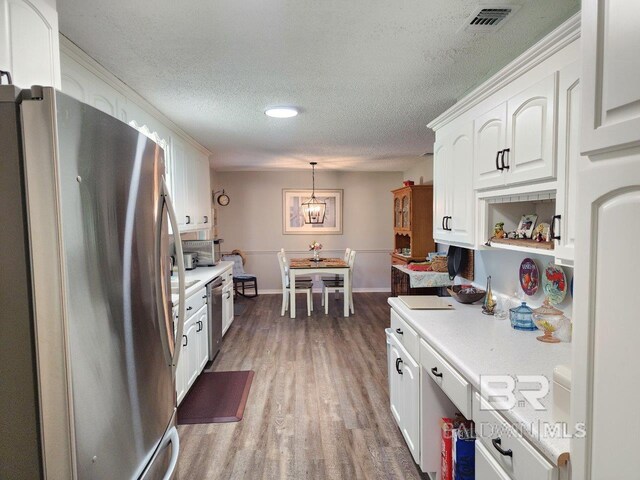 kitchen featuring stainless steel appliances, hardwood / wood-style floors, white cabinetry, a textured ceiling, and hanging light fixtures