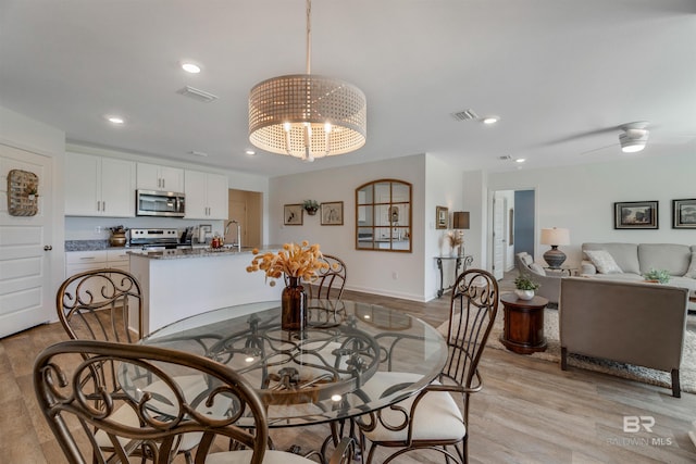 dining area featuring sink, ceiling fan with notable chandelier, and light wood-type flooring