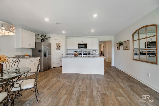 kitchen with white cabinets, light stone counters, light wood-type flooring, and appliances with stainless steel finishes