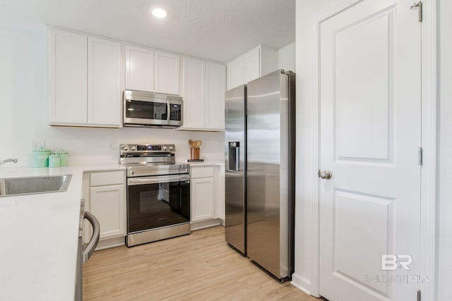 kitchen featuring sink, appliances with stainless steel finishes, white cabinetry, a textured ceiling, and light wood-type flooring