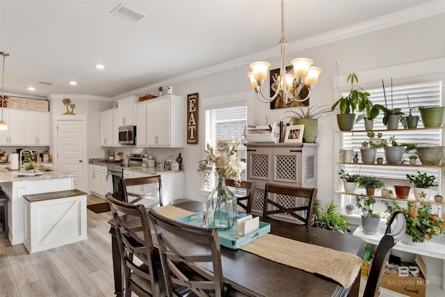 dining room with an inviting chandelier, sink, crown molding, and light hardwood / wood-style floors