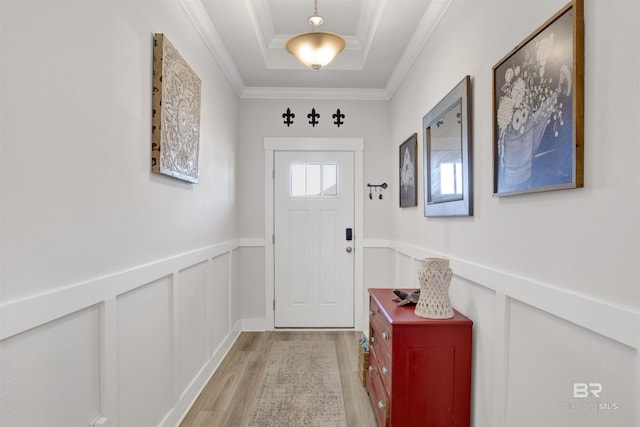 doorway to outside with crown molding, a raised ceiling, and light wood-type flooring