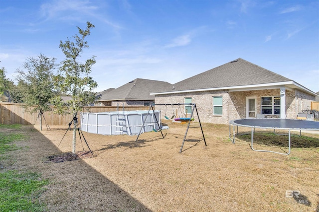 rear view of house featuring a fenced in pool, a trampoline, and a playground