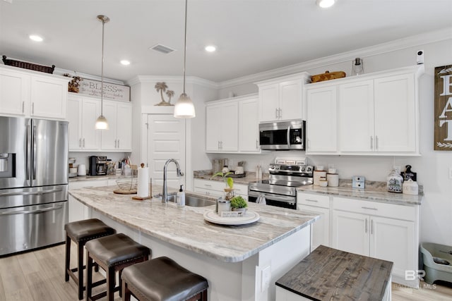 kitchen featuring sink, stainless steel appliances, white cabinets, a center island with sink, and decorative light fixtures