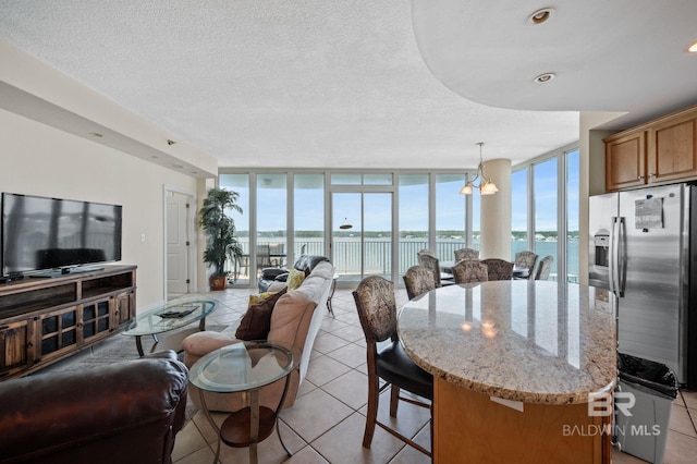 tiled living room featuring plenty of natural light, floor to ceiling windows, and a water view