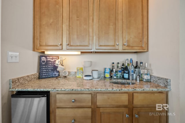 bar featuring light stone counters, fridge, and sink