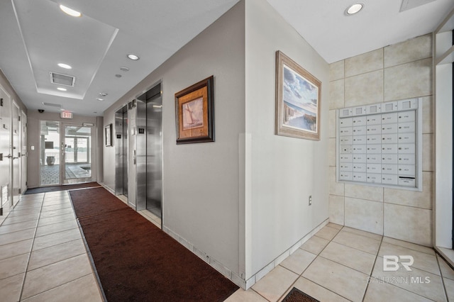 hallway with light tile patterned floors, mail boxes, elevator, and a tray ceiling