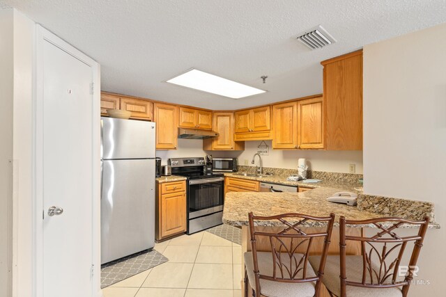 24230 Perdido Beach Blvd Unit 3014, Orange Beach, AL 36561 - kitchen featuring appliances with stainless steel finishes, a sink, a peninsula, under cabinet range hood, and light stone countertops