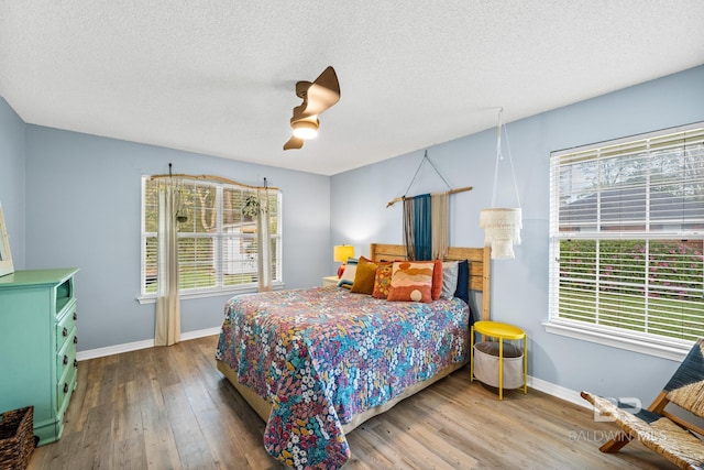 bedroom featuring multiple windows, wood-type flooring, a textured ceiling, and ceiling fan