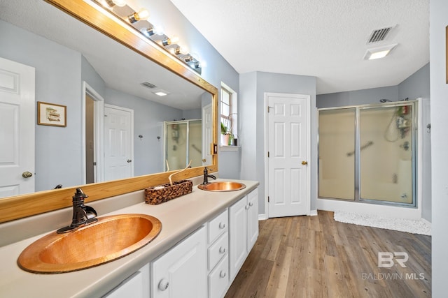 bathroom with vanity, a shower with shower door, a textured ceiling, and wood-type flooring