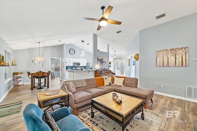 living room with ceiling fan with notable chandelier, lofted ceiling, and light hardwood / wood-style flooring