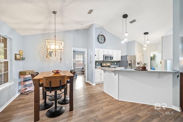 kitchen with white cabinetry, kitchen peninsula, wood-type flooring, decorative backsplash, and appliances with stainless steel finishes