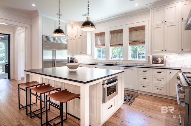 kitchen with premium appliances, a kitchen breakfast bar, pendant lighting, white cabinets, and a center island