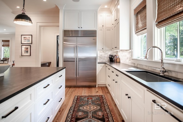 kitchen featuring white cabinetry, stainless steel built in fridge, hanging light fixtures, light hardwood / wood-style flooring, and sink