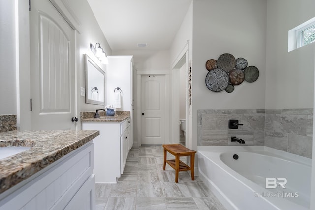 bathroom with a tub to relax in, vanity, and toilet