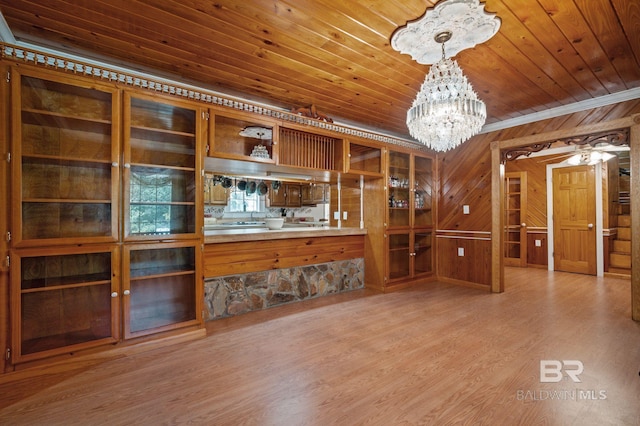 unfurnished living room featuring crown molding, light hardwood / wood-style floors, wooden ceiling, a chandelier, and wood walls