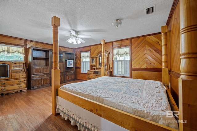 bedroom with ornate columns, crown molding, wood-type flooring, a textured ceiling, and wooden walls