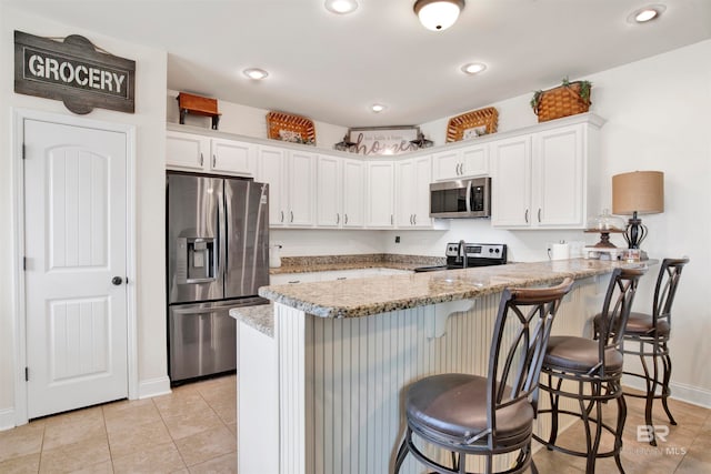 kitchen featuring a breakfast bar area, appliances with stainless steel finishes, white cabinetry, and a peninsula