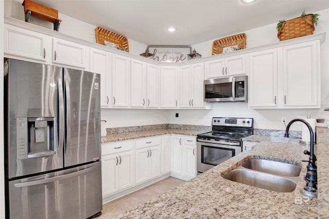 kitchen with a sink, light stone counters, appliances with stainless steel finishes, and light tile patterned floors