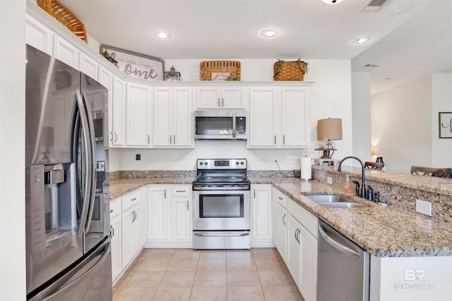 kitchen with a sink, appliances with stainless steel finishes, a peninsula, white cabinets, and light tile patterned floors