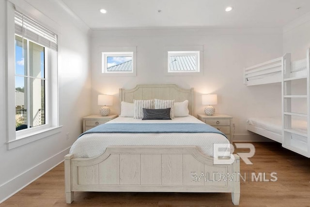 bedroom featuring ornamental molding, wood finished floors, baseboards, and multiple windows