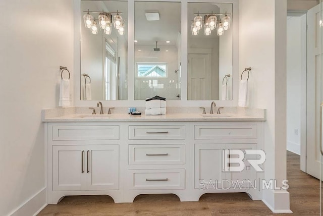 bathroom featuring walk in shower, double vanity, wood finished floors, and a sink