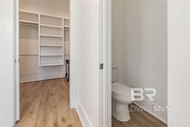 bathroom with a walk in closet, toilet, wood finished floors, and baseboards