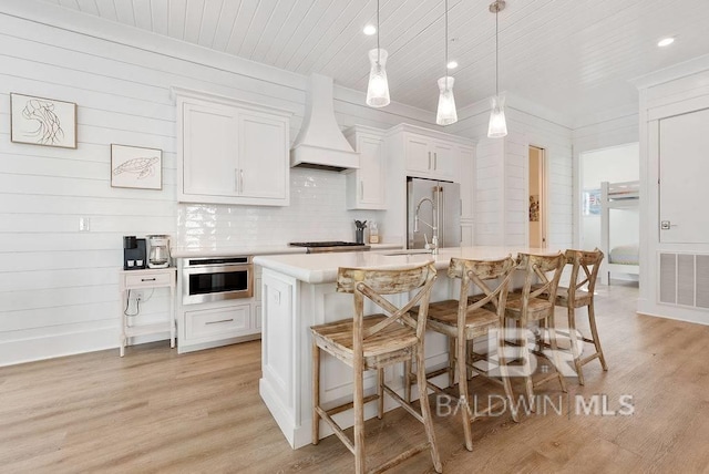 kitchen with visible vents, custom range hood, a kitchen bar, light countertops, and appliances with stainless steel finishes