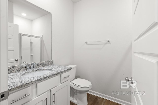 bathroom with toilet, a stall shower, vanity, wood finished floors, and baseboards