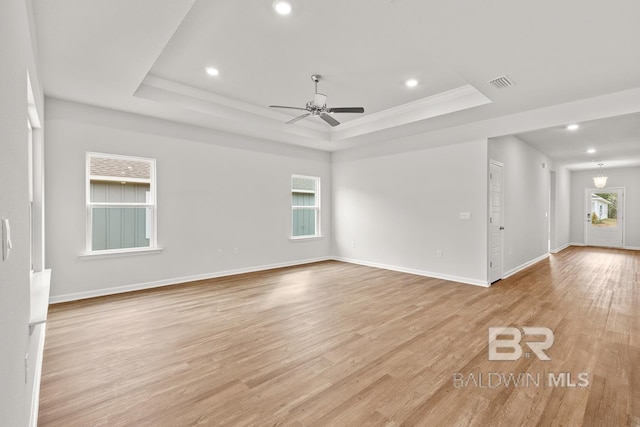 empty room featuring light wood-type flooring, a raised ceiling, and visible vents