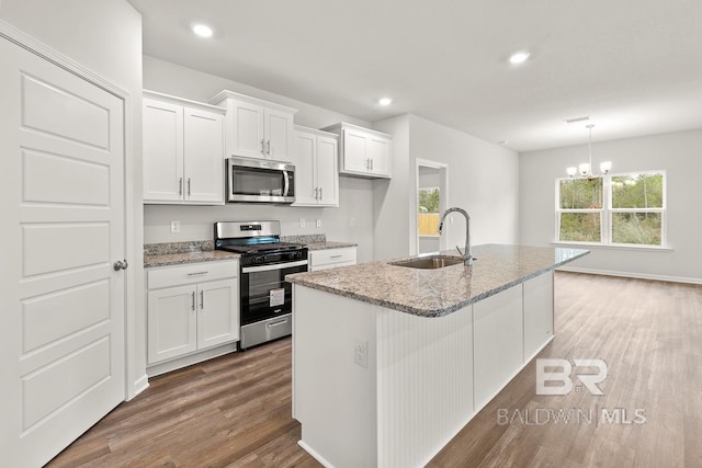 kitchen featuring wood finished floors, appliances with stainless steel finishes, white cabinets, a sink, and light stone countertops