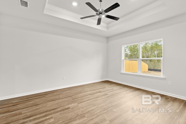 empty room with a tray ceiling, visible vents, ornamental molding, wood finished floors, and baseboards