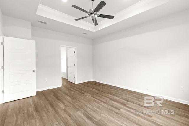 unfurnished bedroom featuring crown molding, a raised ceiling, visible vents, wood finished floors, and baseboards