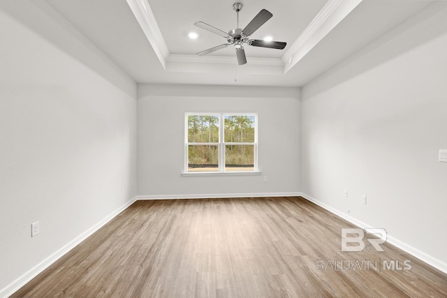 empty room with a raised ceiling, ornamental molding, ceiling fan, wood finished floors, and baseboards